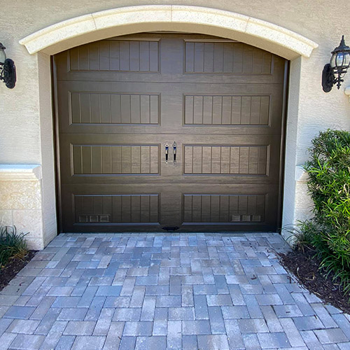 Freshly painted wood-look garage door with paver driveway